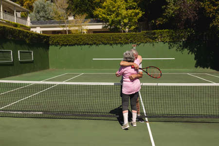 Senior caucasian couple playing tennis together on court embracing. retirement retreat and active senior lifestyle concept.の写真素材