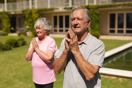 Senior caucasian couple practicing yoga, meditating in sunny garden. retirement retreat and active senior lifestyle concept.の写真素材