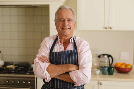 Portrait of senior caucasian man looking at camera and smiling in kitchen. retreat, retirement and happy senior lifestyle concept.の写真素材