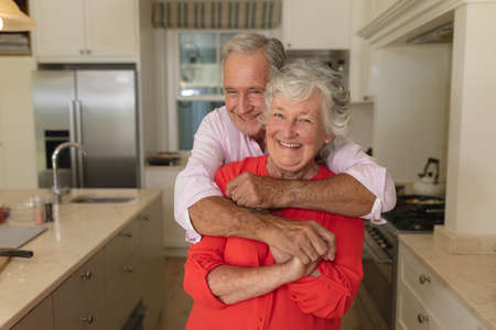 Portrait of senior caucasian couple looking at camera and smiling in kitchen. retreat, retirement and happy senior lifestyle concept.の写真素材