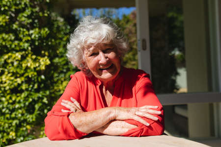 Portrait of senior caucasian woman sitting at table looking at camera and smiling in sunny garden. retreat, retirement and happy senior lifestyle concept.の写真素材