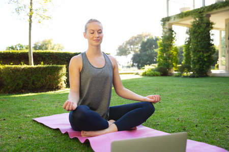 Tranquil caucasian woman practicing yoga in sunny garden, sitting and meditating with eyes closed....