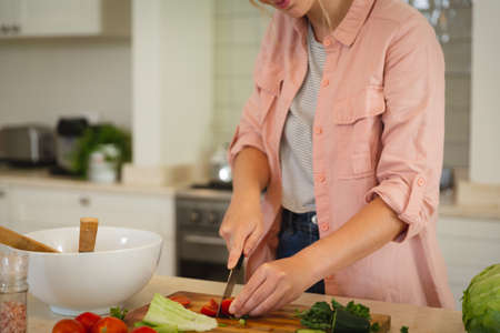 Midsection of caucasian woman standing in kitchen preparing food, chopping vegetables. spending free...