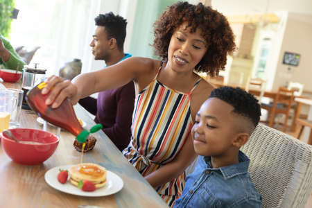 Happy african american family sitting at table smiling during breakfast. family enjoying quality free time together.の写真素材
