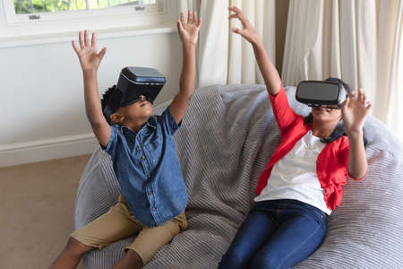 Happy african american boy and girl using vr headsets and smiling at home. childhood with...