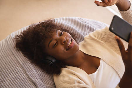 Happy african american woman lying on beanbag making video call with smartphone and smiling....
