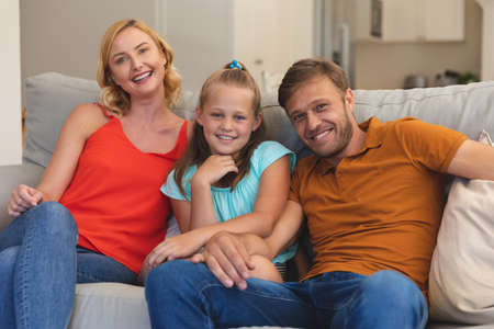 Portrait of caucasian couple with daughter sitting on couch and smiling at home. family enjoying...