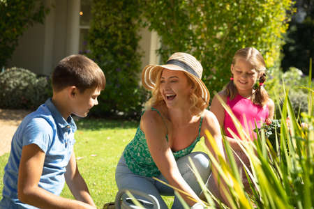 Happy caucasian mother with son and daughter outdoors, gardening on sunny day. family enjoying...