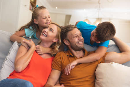 Caucasian couple with daughter and son sitting on couch and smiling at home. family enjoying quality free time together.の写真素材