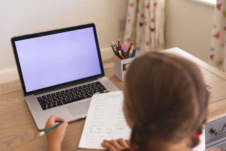 Caucasian girl having video call during class on laptop with copy space, sitting at desk at home....