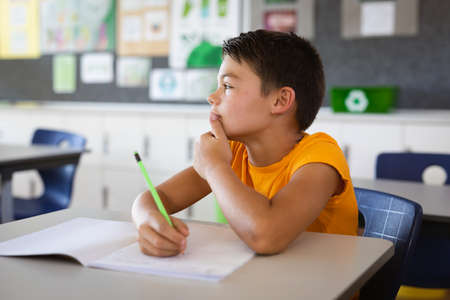 Caucasian boy studying while sitting on his desk in the class at school. school and education...