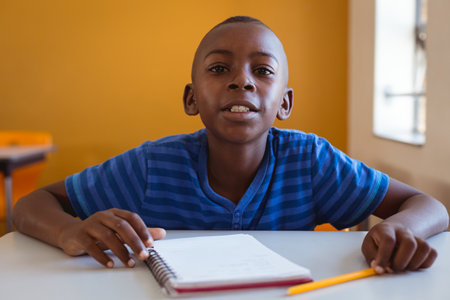 Portrait of african american schoolboy sitting at desk with notebook in classroom. childhood and education at elementary school.の写真素材