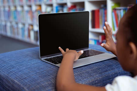 African american schoolgirl at desk in school library using laptop, with copy space on screen....
