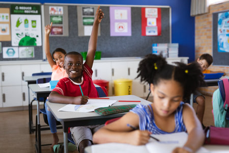 African american boy and girl raising their hands while sitting in the class at elementary school. school and education conceptの写真素材