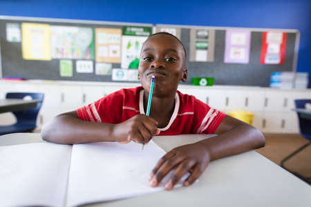 Portrait of african american boy sitting on his desk in the class at elementary school. school and...