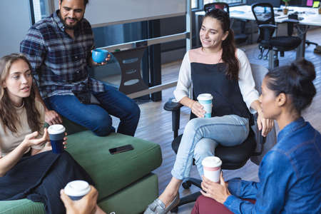 Diverse group of creative colleagues holding takeaway coffees, talking at casual meeting. modern office of a creative design business.の写真素材