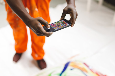African american male painter at work taking picture of artwork with smartphone in art studio. creation and inspiration at an artists painting studio.の写真素材