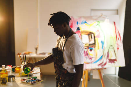African american male painter at work holding paint in art studio. creation and inspiration at an artists painting studio.の写真素材