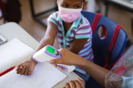 Mid section of female health worker measuring temperature of a girl at elementary school. education...