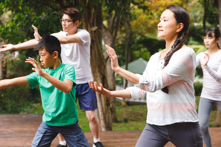 Asian parents, son and daughter exercising outdoors, practicing tai chi. family fitness time in garden.の写真素材