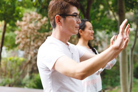 Asian couple wearing white shirts exercising outdoors, practicing tai chi. family fitness time in garden.の写真素材