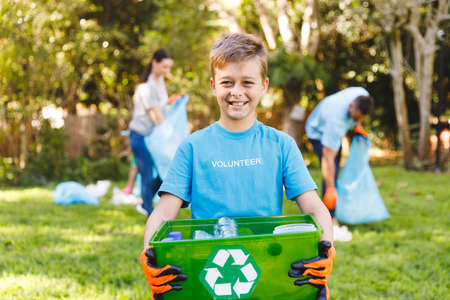 Portrait of smiling caucasian son holding recycling box, cleaning up countryside with parents. eco conservation volunteers, countryside clean-up.の写真素材