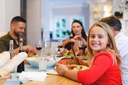 Portrait of caucasian grandfather and parents with daughter sitting at table having dinner. family...