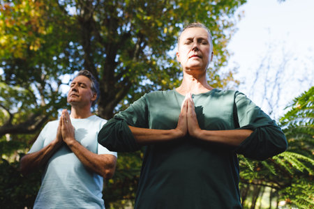 Peaceful senior caucasian couple practicing yoga, meditating in sunny garden. healthy retirement lifestyle, spending time at home.の写真素材