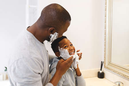 African american father with son having fun with shaving foam in bathroom. family spending time at home.の写真素材