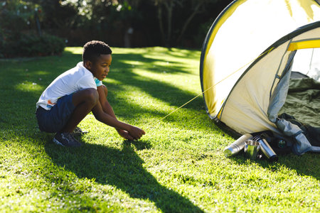 African american boy having fun pitching tent with ropes in sunny garden. spending time at home.の写真素材
