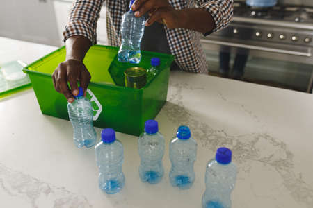 Hands of african american man in kitchen sorting rubbish into crate for recycling. family spending time at home.の写真素材
