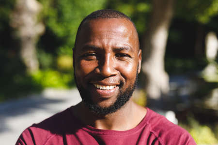Portrait of african american man smiling and looking at camera in sunny garden. spending time alone...