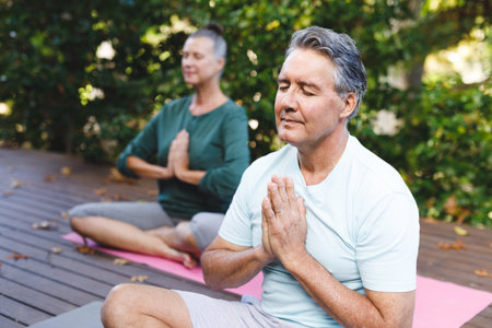 Happy senior caucasian couple practicing yoga, meditating in sunny garden. healthy retirement lifestyle, spending time at home.の写真素材