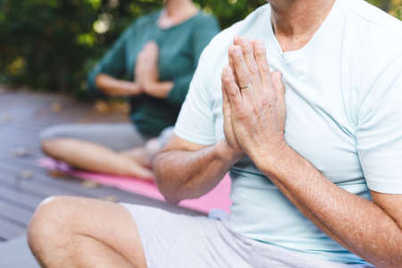 Midsection of senior caucasian couple practicing yoga, meditating in sunny garden. healthy retirement lifestyle, spending time at home.の写真素材