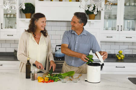 Happy senior caucasian couple in modern kitchen, cooking together composting organic waste....