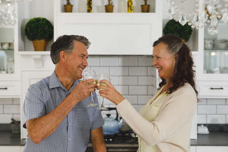 Happy senior caucasian couple in modern kitchen, drinking wine, making a toast and smiling....