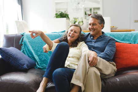 Happy senior caucasian couple in living room sitting on sofa, embracing. retirement lifestyle, spending time at home.の写真素材