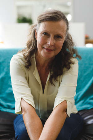 Portrait of happy senior caucasian woman in living room sitting on sofa, looking to camera....