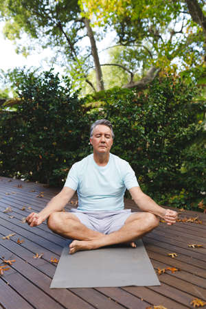 Relaxed senior caucasian man practicing yoga, meditating in garden. healthy retirement lifestyle, spending time self caring at home.の写真素材