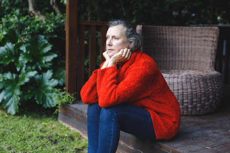 Thoughtful senior caucasian woman sitting and looking away in garden. retirement lifestyle, spending time alone at home.の写真素材