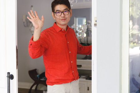 Portrait of asian man standing at door and waving hand to visitor. hospitality and welcoming guests...