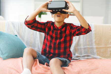 Smiling asian boy sitting on couch and using vr headset. childhood leisure time and discovery using...