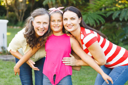 Portrait of smiling caucasian grandmother with adult daughter and granddaughter in garden. multi...