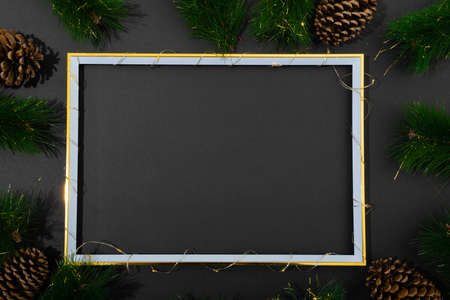 Composition of frame with copy space and fir tree branches with pine cones on black background....