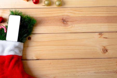 Composition of christmas stocking with fir tree, smartphone and copy space on wooden background. christmas, tradition and celebration concept.の写真素材
