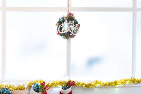 Composition of merry christmas sign in window, with christmas stockings. christmas, tradition and celebration concept.の写真素材