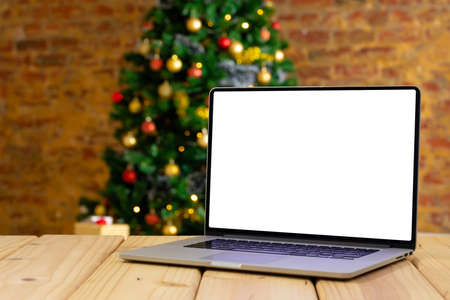 Composition of laptop with copy space on wooden table with christmas tree in background. christmas, communication, tradition and celebration concept.の写真素材