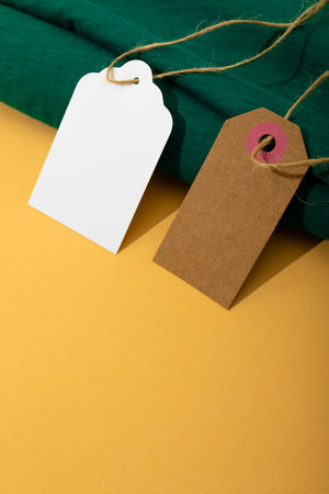 Composition of gift tags with copy space and green fabric on yellow background. christmas, gifts, tradition and celebration concept.の写真素材