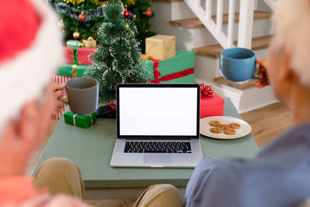 Back view of caucasian senior couple using laptop, having video call at christmas time. christmas,...