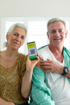 Smiling caucasian senior couple showing smartphone with covid vaccine passport on screen. senior health and lifestyle during covid 19 pandemic.の写真素材